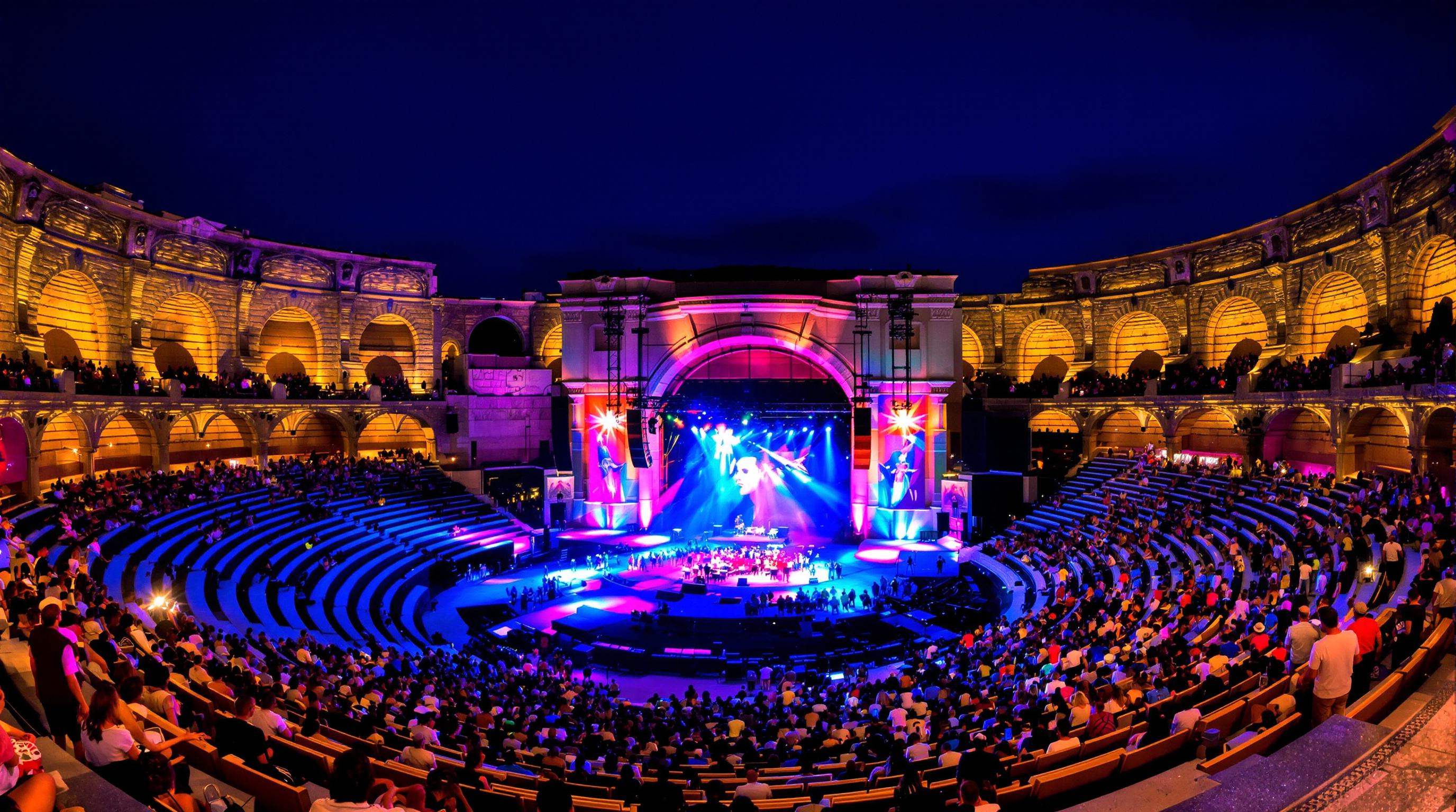 Concert nocturne dans les Arènes d'Arles, lumière colorée sur la pierre et foule contemporaine