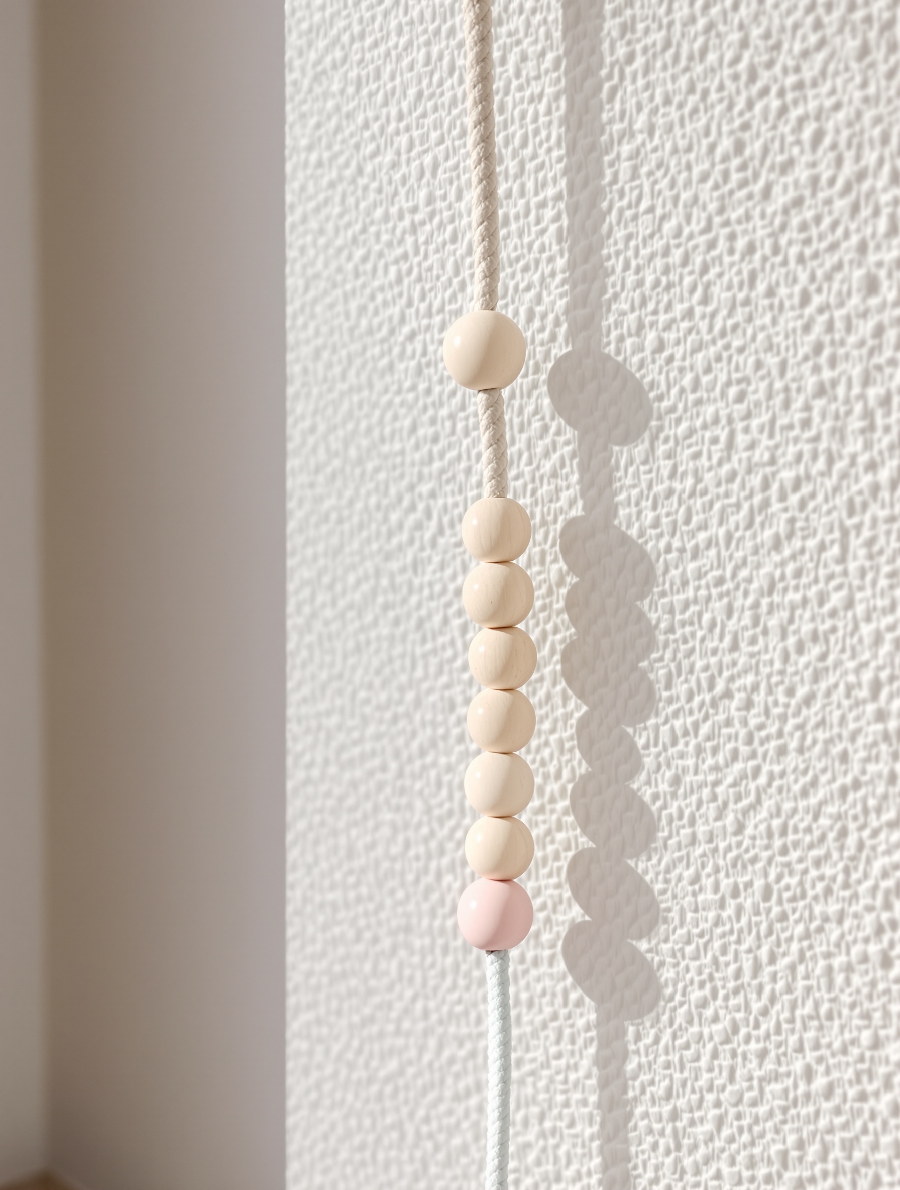 Câble customisé avec perles en bois et cordelette pastel sur mur scandinave chic et créatif