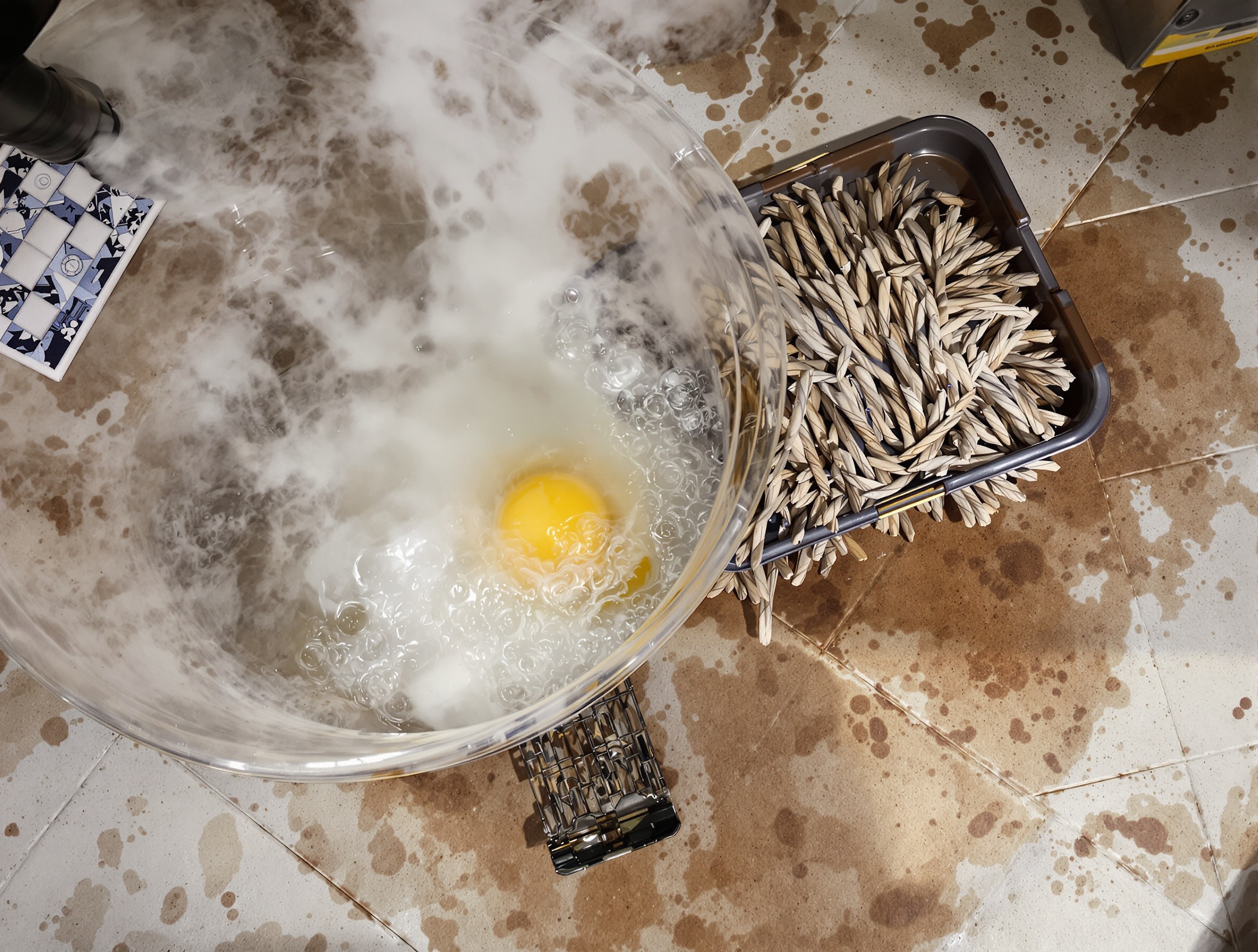 Seau d'eau chaude avec pastille dissoute, serpillière et carrelage en cours de nettoyage.